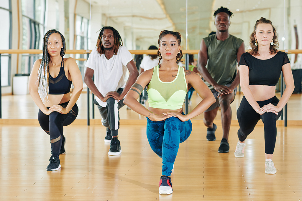 Group of concentrated sporty fit young people doing lunges when working out indoors together
