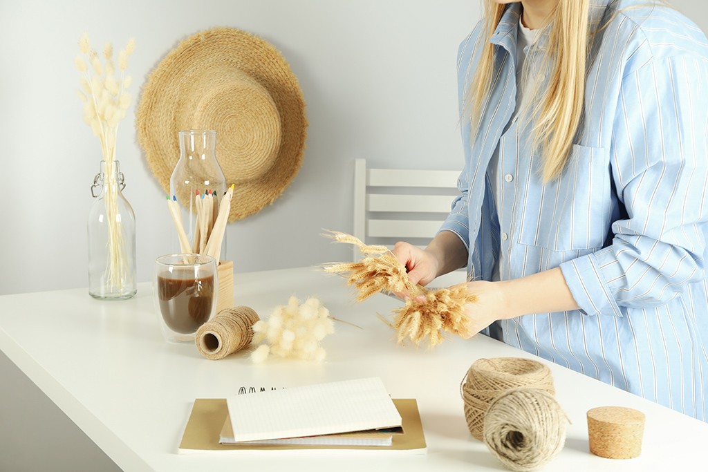 woman putting together decorations with artificial plants, twine and paper on a desk