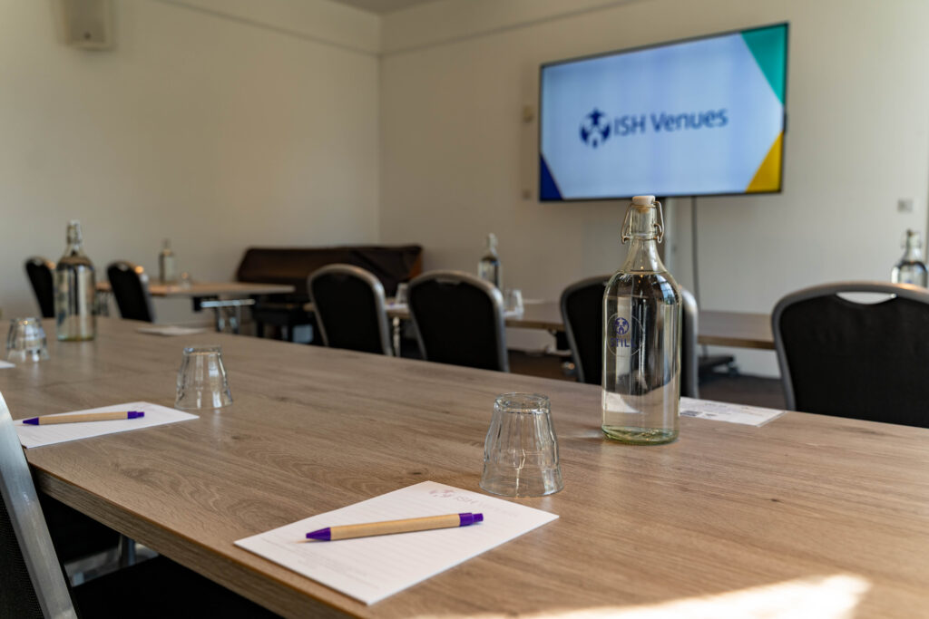 Classroom layout in the Gulbenkian Room at ISH Venues with a notepad, pen and water set out on the table.