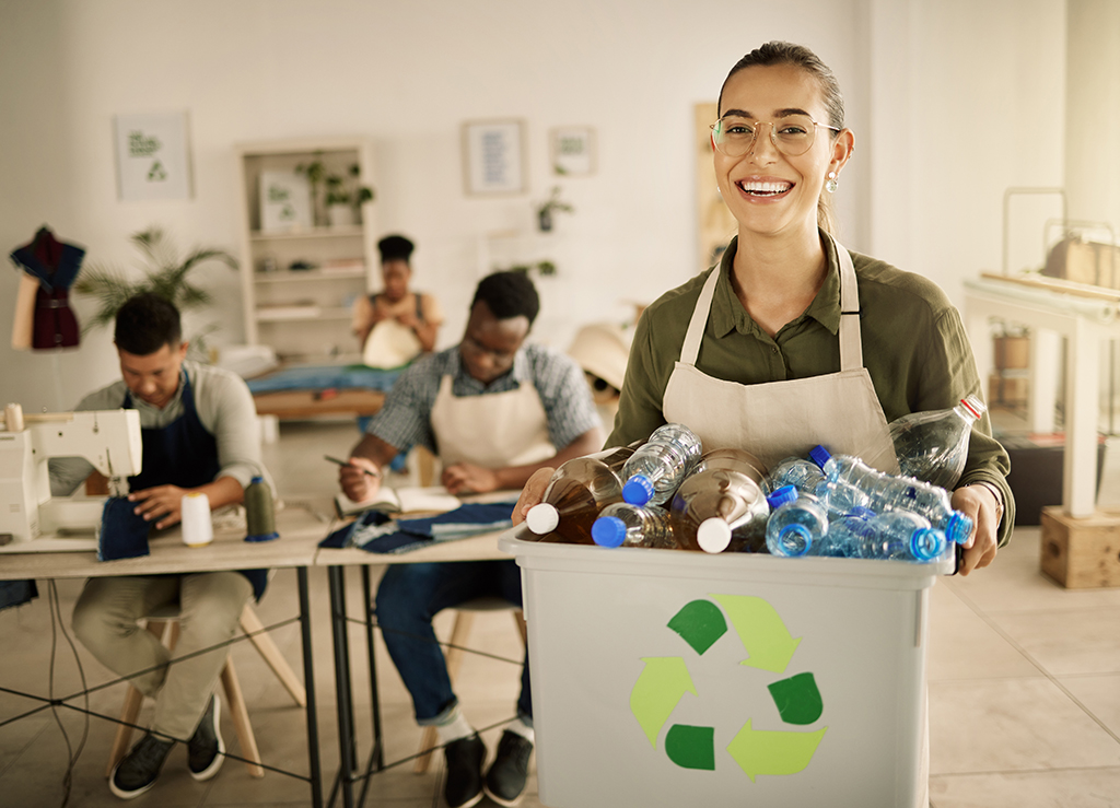 Cheerful woman holding a bucket of recycled plastic bottles.