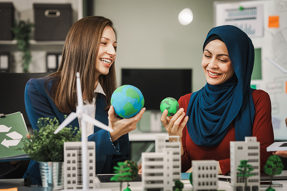 Women holding up Earth globes with a sustainable city model in front of them on the table.