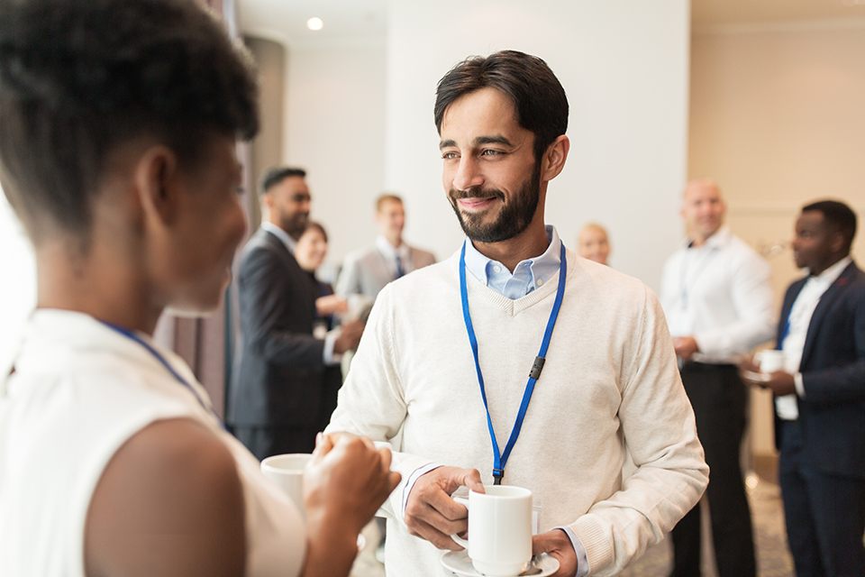 business, communication and education concept - international group of people with conference badges drinking coffee and talking